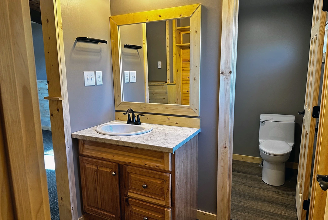 Modern campground bathroom vanity featuring custom wood cabinetry with marble countertop and framed mirror, showcasing True North Construction's quality craftsmanship for Sky Ranch Campground facilities
